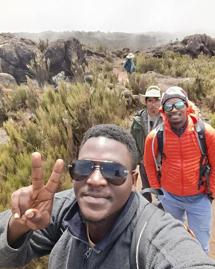 Three hikers on Kilimanjaro moorland with heather, rocks and low cloud behind them