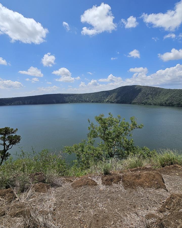 Lake Chala, a calm crater lake ringed by forested hills under a blue sky with scattered clouds