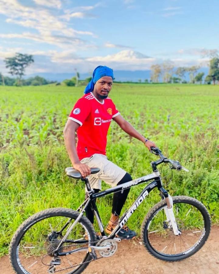 A cyclist on a mountain bike beside a green field with the snowy top of Kilimanjaro on the horizon